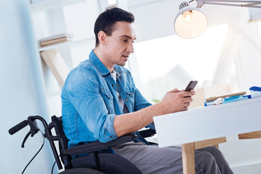 Just attention. Serious man sitting in the wheelchair and bowing head while looking at telephone