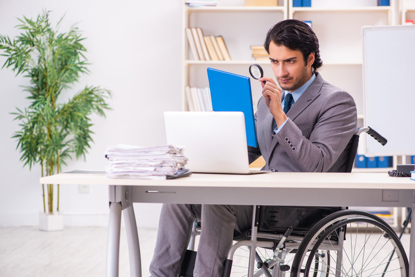 Young handsome employee in wheelchair at the office