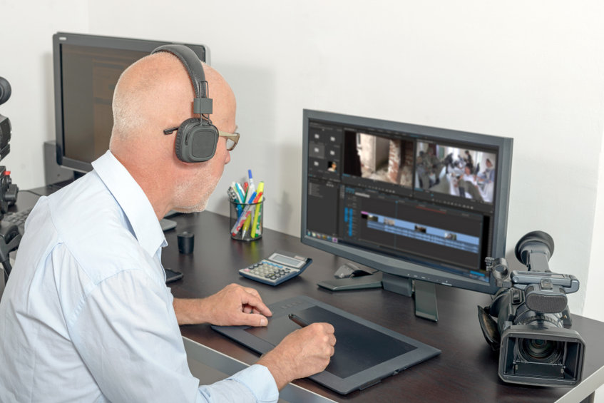 person with headphones on works in front of a computer with video editing software