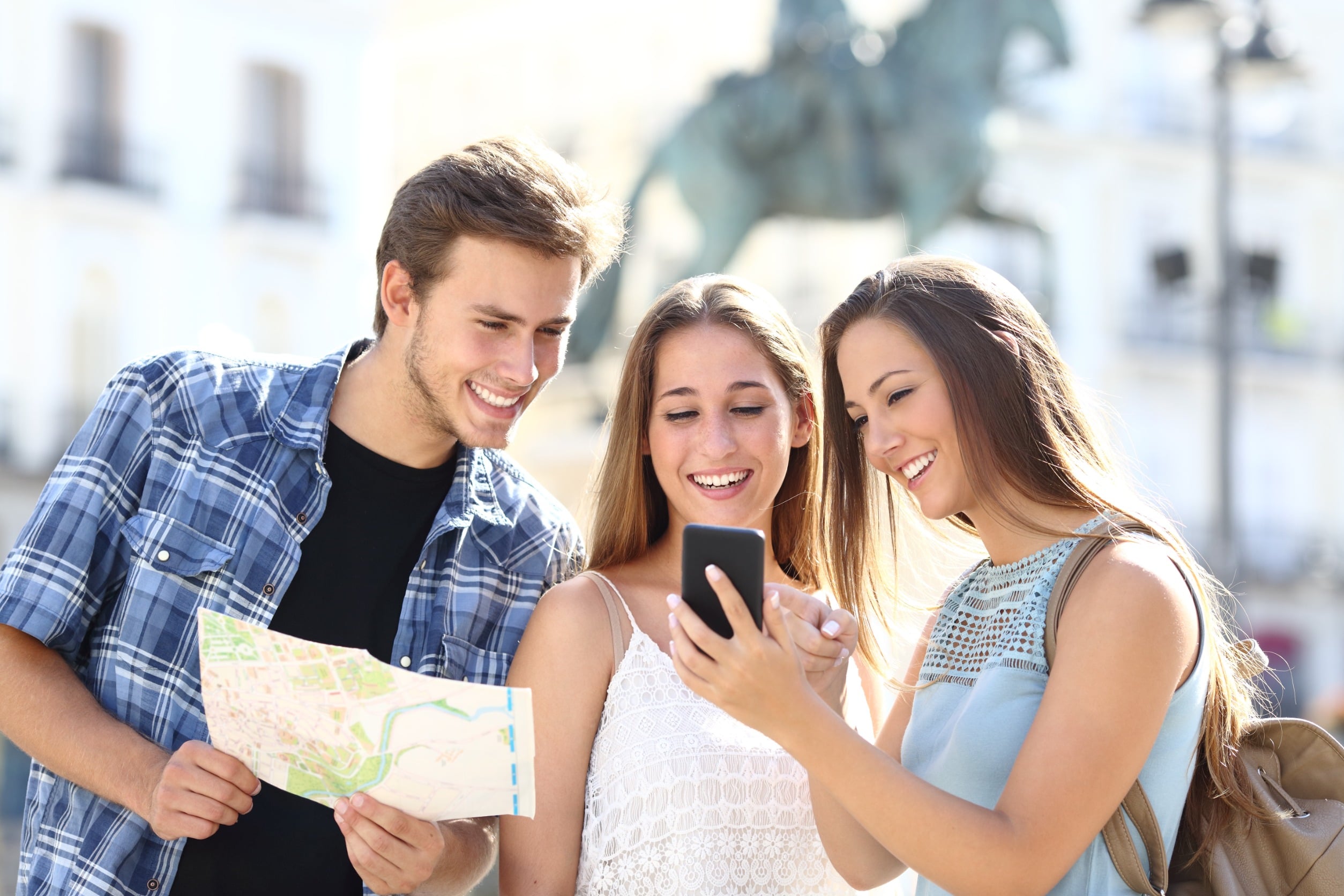 Un grupo de jóvenes formado por dos chicas y un chico, se encuentran en la calle revisando juntos un mapa y consultando un móvil