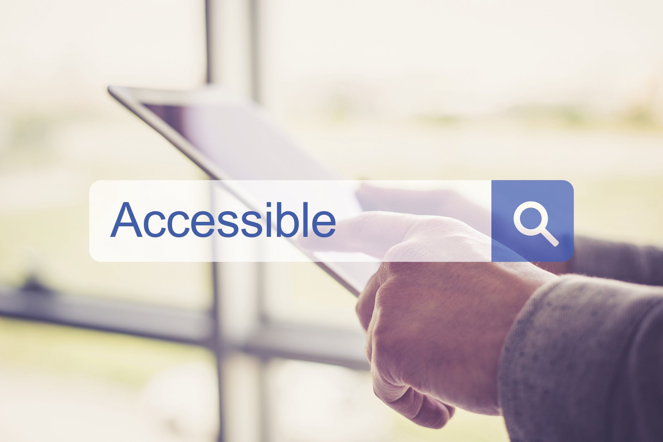 Casella di ricerca con la parola "accessible" in inglese, sullo sfondo vediamo delle mani che interagiscono con un tablet elettronico.
