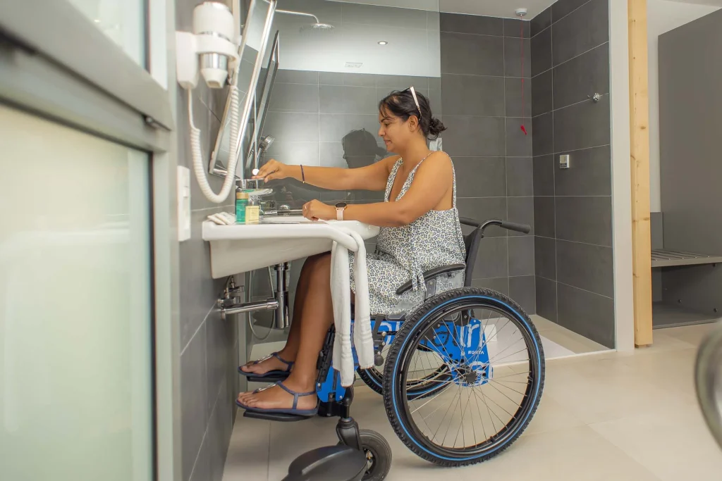 Una chica sobre silla de ruedas hace uso del lavabo dentro del baño de una de las habitaciones adaptadas del Hotel Taimar.