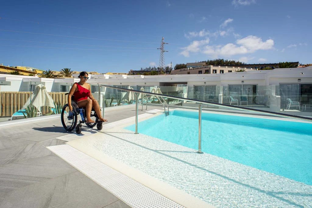 Una chica sobre silla de ruedas hace uso de una rampa que la lleva a una piscina adaptada del Hotel Taimar.